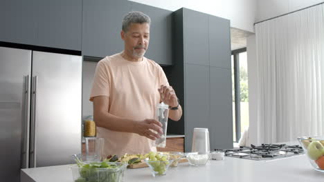 Happy-senior-biracial-man-preparing-healthy-smoothie-in-kitchen-at-home,-copy-space,-slow-motion