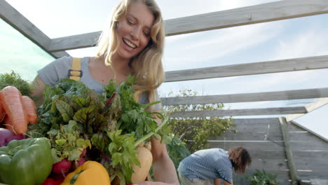 Happy-diverse-couple-holding-basket-of-fresh-vegetables-and-working-in-garden,-slow-motion