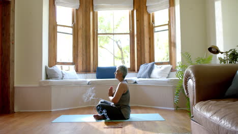 Mujer-Birracial-Senior-Enfocada-Meditando-En-Una-Estera-De-Yoga-En-Casa