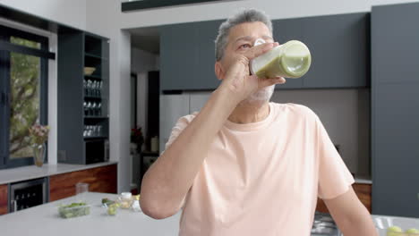 Senior-biracial-man-drinking-healthy-smoothie-in-kitchen-at-home,-copy-space,-slow-motion