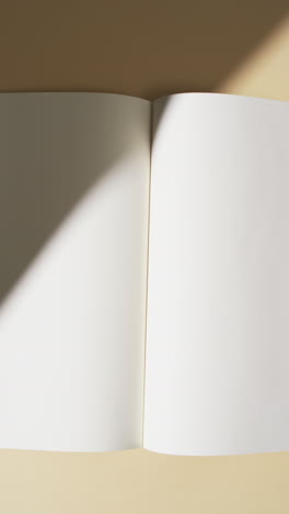 Vertical-video-of-shadow-over-book-with-blank-pages-and-copy-space-on-yellow-background