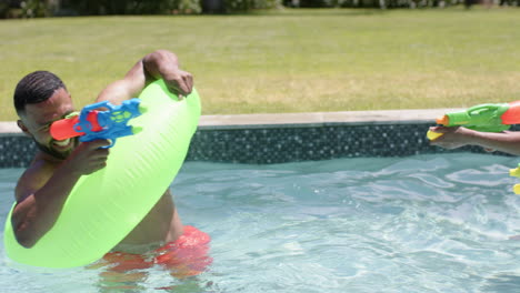 Happy-african-american-parents-and-daughter-playing-with-water-pistols-in-sunny-pool,-slow-motion