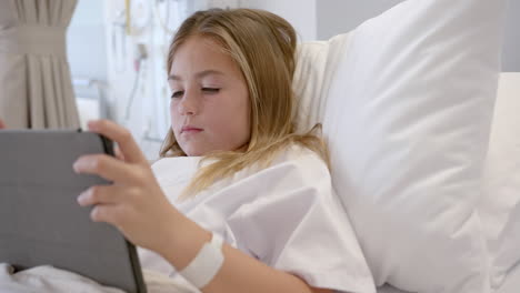 Caucasian-girl-patient-sitting-up-in-hospital-bed-using-tablet,-slow-motion