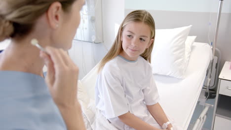 Caucasian-female-doctor-using-stethoscope-on-chest-of-girl-patient-on-hospital-bed,-slow-motion