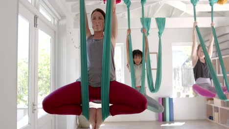Focused-diverse-fitness-women-exercising-in-aerial-yoga-class-in-big-white-room,-slow-motion