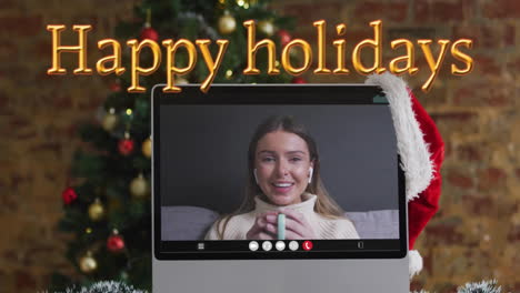Animation-of-happy-holidays-text-over-christmas-tree-and-caucasian-woman-on-laptop-screen