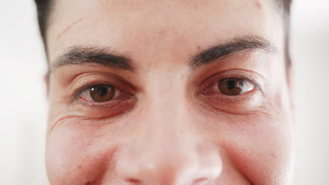 Portrait-close-up-of-brown-eyes-of-happy-biracial-man-smiling-at-home,-slow-motion