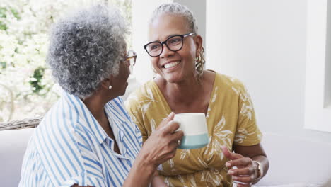 Glückliche-ältere-Afroamerikanische-Freundinnen,-Die-Kaffee-Trinken-Und-Im-Wohnzimmer-Lachen,-Zeitlupe