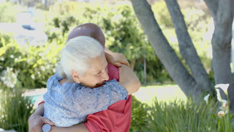 Happy-senior-biracial-couple-embracing-in-sunny-garden-at-home,-slow-motion