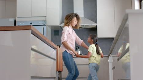 Happy-biracial-mother-and-daughter-having-fun-dancing-together-in-kitchen,-copy-space,-slow-motion