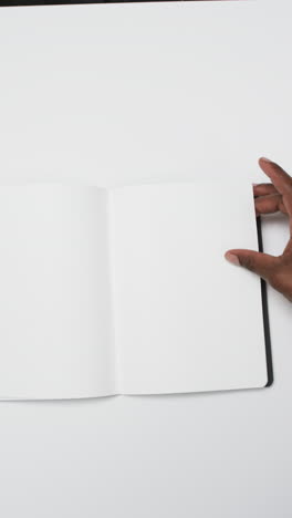 Vertikales-Video-Der-Hand-Eines-Afroamerikanischen-Mannes-Mit-Einem-Buch-Mit-Weißen-Leeren-Seiten-Auf-Weißem-Hintergrund