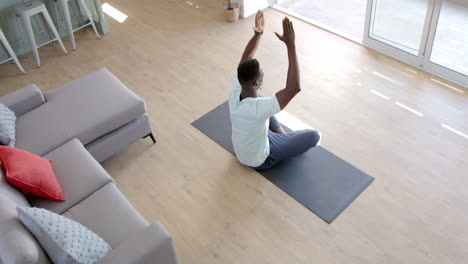 Fokussierter-Afroamerikanischer-Mann-Praktiziert-Yoga-Meditation-Im-Sonnigen-Wohnzimmer,-Zeitlupe