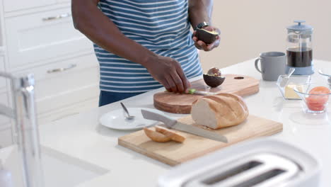 African-american-man-preparing-avocado-toasts-in-sunny-kitchen,-slow-motion