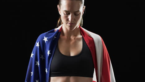 Young-Caucasian-athlete-woman-draped-in-an-American-flag-on-a-black-background