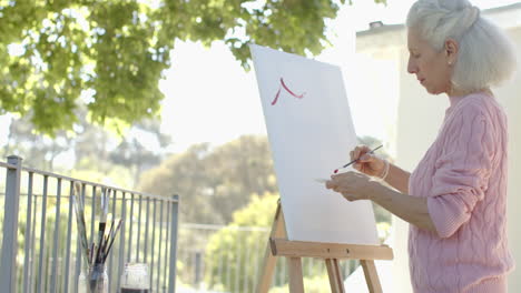 Happy-senior-biracial-woman-painting-at-balcony-at-home,-slow-motion