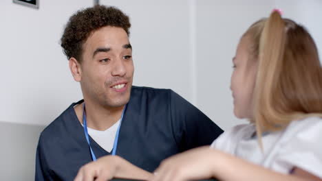 Young-biracial-male-nurse-in-medical-scrubs-interacts-with-a-Caucasian-girl