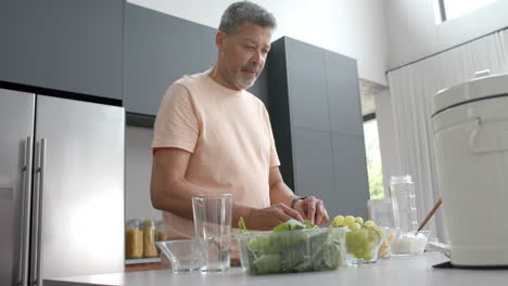 Glücklicher-älterer-Mann-Mit-Gemischter-Abstammung,-Der-In-Der-Küche-Zu-Hause-Zutaten-Für-Einen-Gesunden-Smoothie-Zubereitet,-Zeitlupe