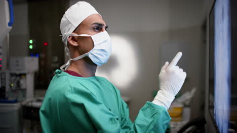 Cirujano-Masculino-Birracial-Mirando-Con-Exploraciones-De-Rayos-X-En-El-Quirófano-Del-Hospital,-Cámara-Lenta