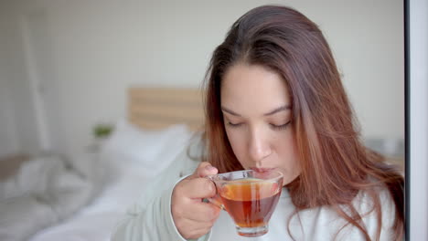 Thoughtful-plus-size-biracial-woman-having-tea-in-bedroom,-looking-up,-copy-space,-slow-motion