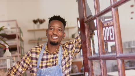 Happy-african-american-male-potter-standing-in-shop-entrance-and-smiling,-slow-motion