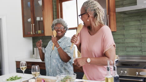 Glückliche-ältere-Afroamerikanische-Freundinnen-Bereiten-Essen-Zu-Und-Singen-In-Der-Küche,-Zeitlupe
