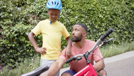 Feliz-Padre-Afroamericano-Enseñando-A-Su-Hijo-Sobre-Bicicleta-En-El-Jardín,-Cámara-Lenta