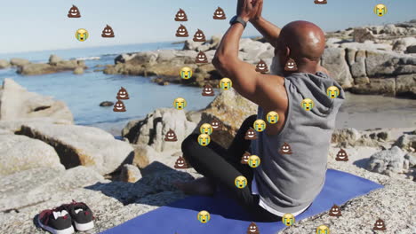Animation-of-emoji-icons-over-senior-african-american-man-meditating-on-beach