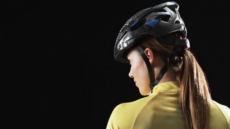 Young-Caucasian-woman-cyclist-in-cycling-gear,-with-copy-space-on-black-background
