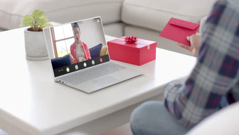 Caucasian-man-holding-red-envelope-using-laptop-with-biracial-woman-opening-gift-on-screen