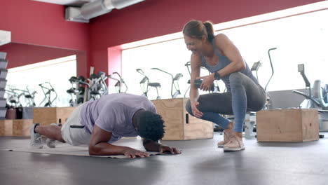 Fit-African-American-man-does-a-plank-at-the-gym-with-trainer,-with-copy-space