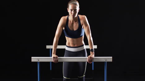 Young-Caucasian-woman-performs-a-dip-exercise-on-hurdles-at-the-gym-on-a-black-background