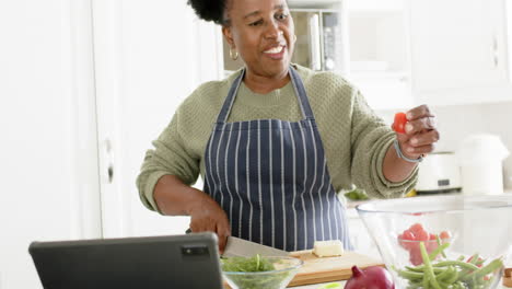 Glückliche-Afroamerikanische-Seniorin,-Die-Gemüse-Hackt-Und-In-Der-Sonnigen-Küche-Tanzt,-Zeitlupe