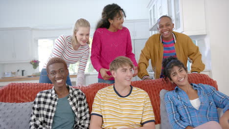 Happy-diverse-group-of-teenage-friends-sitting-on-couch-and-laughing-at-home,-slow-motion
