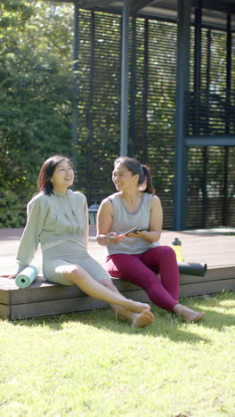Happy-asian-female-friends-with-exercise-mats-using-smartphone-on-sunny-terrace,-slow-motion