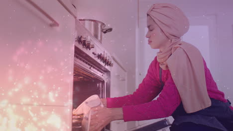 Biracial-woman-in-hijab-taking-out-tray-of-chopped-vegetables-from-oven,-cooking-over-spots-of-light