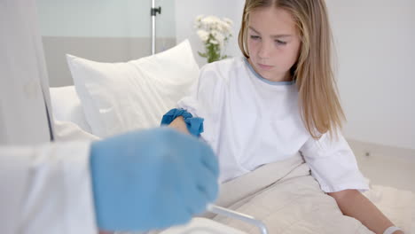 Diverse-male-doctor-taking-blood-sample-from-girl-patient-in-bed-with-syringe,-slow-motion