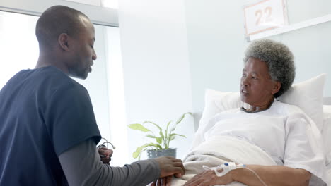 African-american-male-doctor-talking-with-female-senior-patient-in-hospital-room,-slow-motion