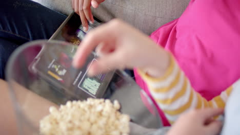 Diverse-teenage-female-friends-using-tablet-with-movies-and-eating-popcorn-at-home,-slow-motion