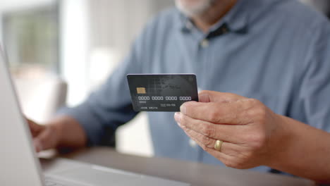 Glücklicher-älterer-Mann-Mit-Gemischter-Abstammung,-Der-Kreditkarte-Und-Laptop-Für-Online-Zahlungen-Verwendet,-Zeitlupe