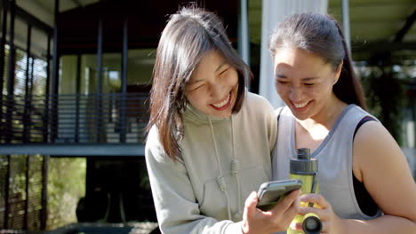 Glückliche-Asiatische-Freundinnen-Mit-Wasserflasche-Und-Smartphone-Lachen-Auf-Der-Terrasse,-Zeitlupe