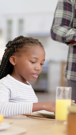 Vertical-video-of-happy-african-american-girl-with-father-having-breakfast-at-home,-slow-motion