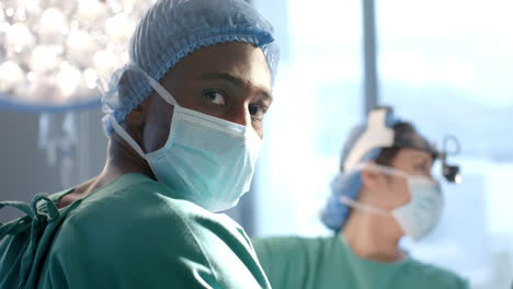 Portrait-of-african-american-male-surgeon-operating-with-colleagues-in-theatre,-slow-motion