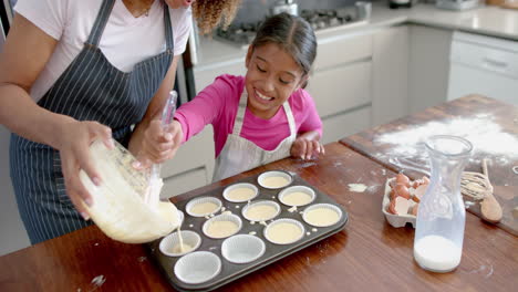 Happy-biracial-mother-and-daughter-pouring-cake-mix-into-forms-in-kitchen,-copy-space,-slow-motion