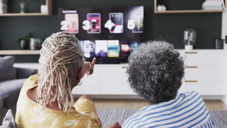 Ältere-Afroamerikanische-Freundinnen-Auf-Der-Couch-Wählen-Aus,-Was-Sie-Im-Fernsehen-Sehen-Möchten,-Zeitlupe