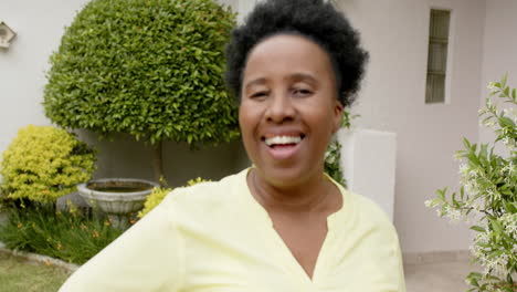 Glückliche-Afroamerikanische-Seniorin-Mit-Lockigem-Haar,-Die-Im-Sonnigen-Garten-Lacht,-Zeitlupe