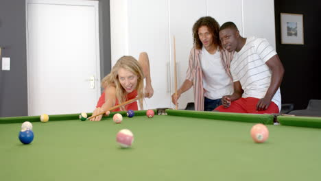 Young-Caucasian-woman-plays-pool-at-home,-flanked-by-diverse-friends