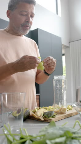 Vertical-video-of-senior-biracial-man-preparing-smoothie-in-kitchen-at-home