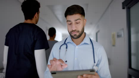 Young-Asian-doctor-in-medical-attire-reviews-patient-data-on-a-tablet