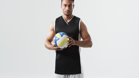 Young-biracial-man-holding-a-volleyball-on-a-white-background,-with-copy-space