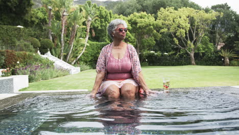 Glückliche-ältere-Afroamerikanische-Frau,-Die-Im-Garten-Sitzt-Und-Im-Pool-Planscht,-Kopierraum,-Zeitlupe